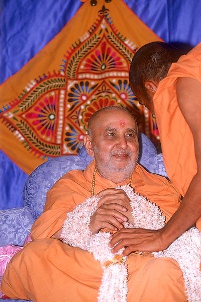 Pujya Dharmakuvar Swami, the local Kothari, honors Swamishri with a garland  	