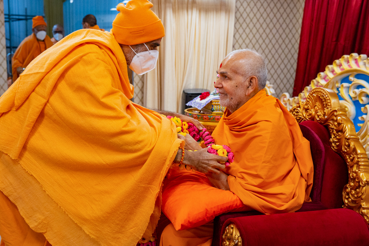 Anandswarup Swami honors Swamishri with a garland