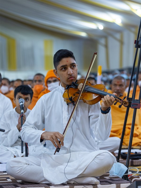 A youth plays a violin in Swamishri's daily puja