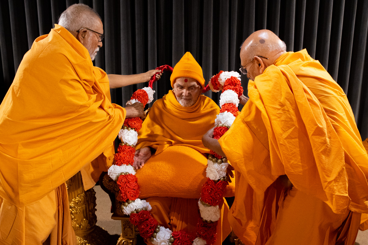 Pujya Kothari Swami and Pujya Tyagvallabh Swami honor Swamishri with a garland