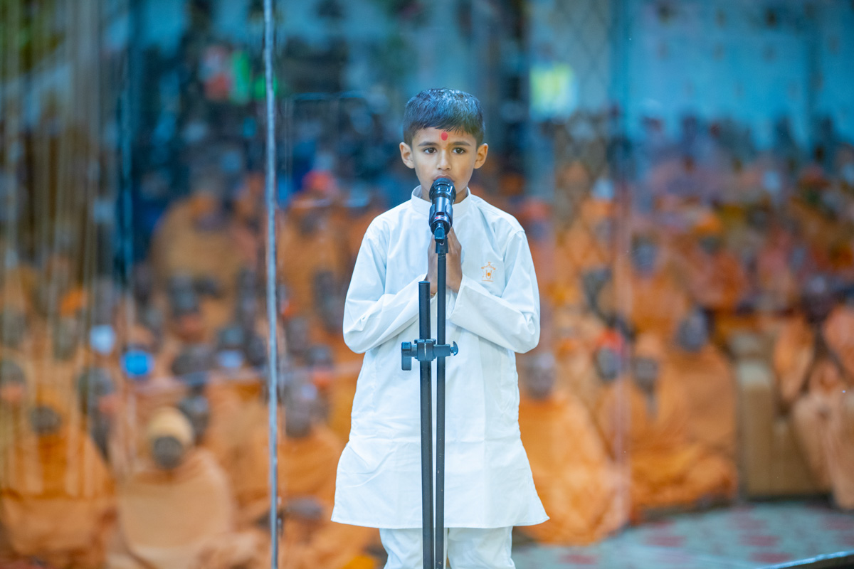 A child leads everyone in reciting the sadhana mantra and daily prayer in Swamishri's puja 