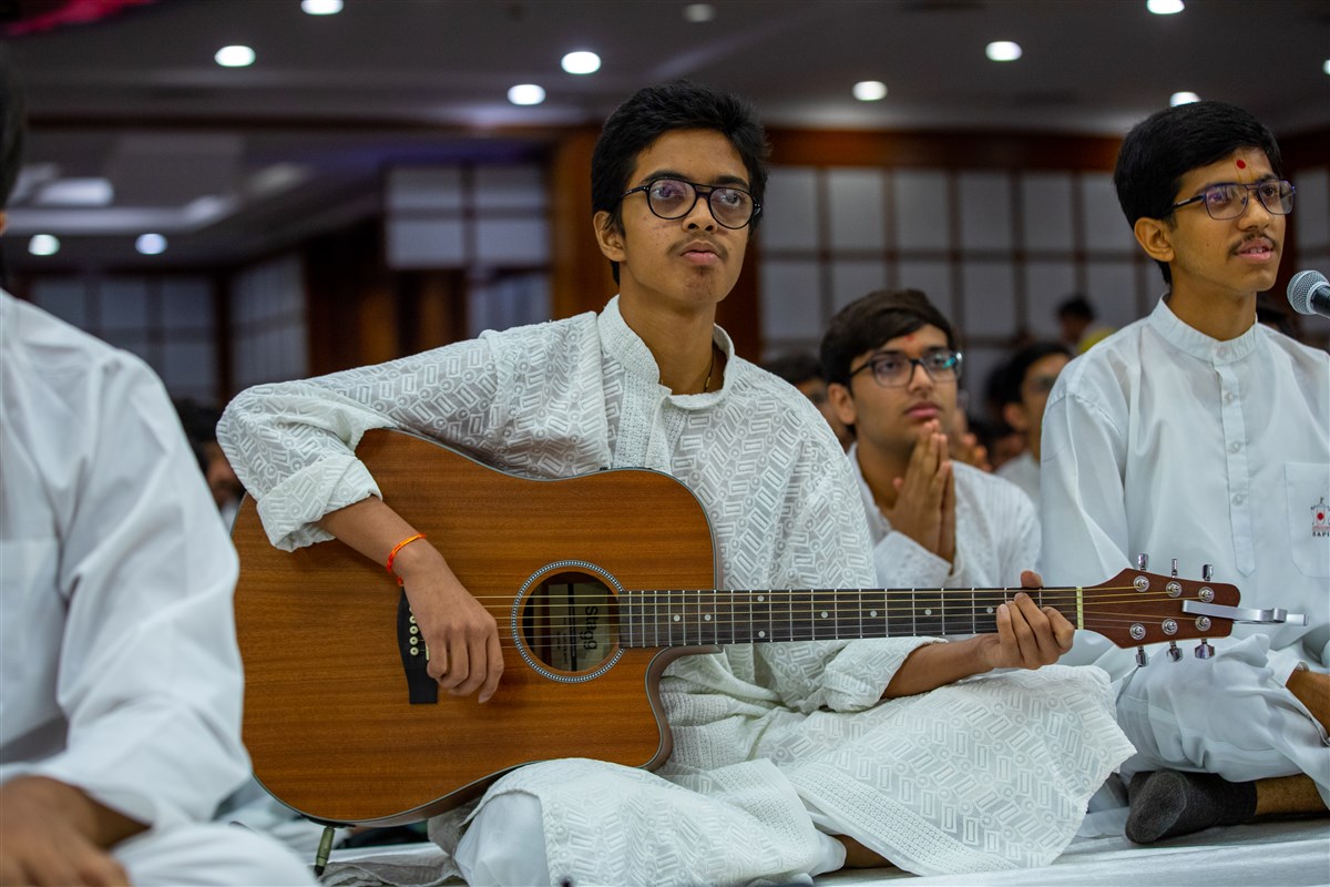 A youth plays the guitar in Swamishri's daily puja