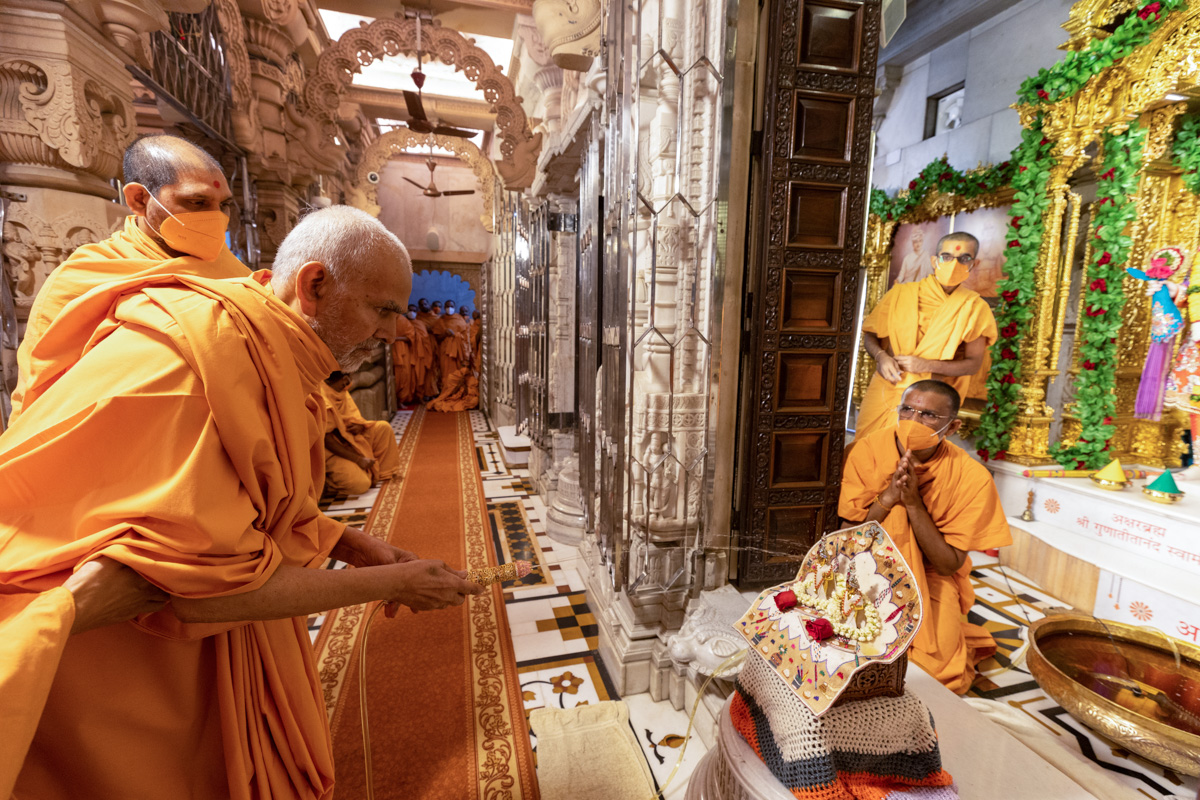 Swamishri sprays saffron-scented water on Shri Harikrishna Maharaj and Shri Gunatitanand Swami