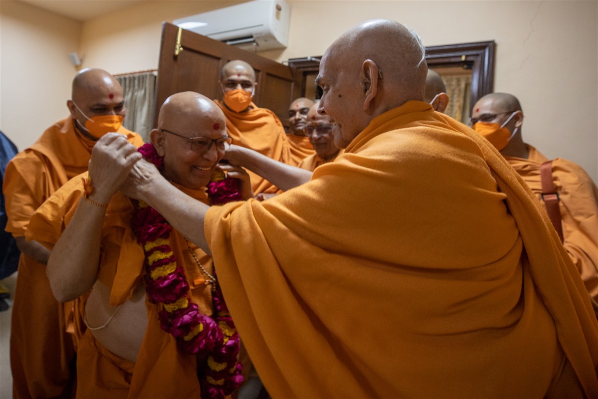 Swamishri honors Pujya Ghanshyamcharan Swami with a garland