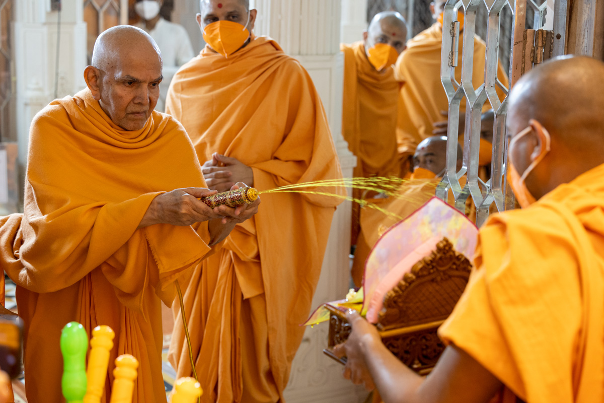 Swamishri sprays saffron-scented water on Shri Akshar-Purushottam Maharaj