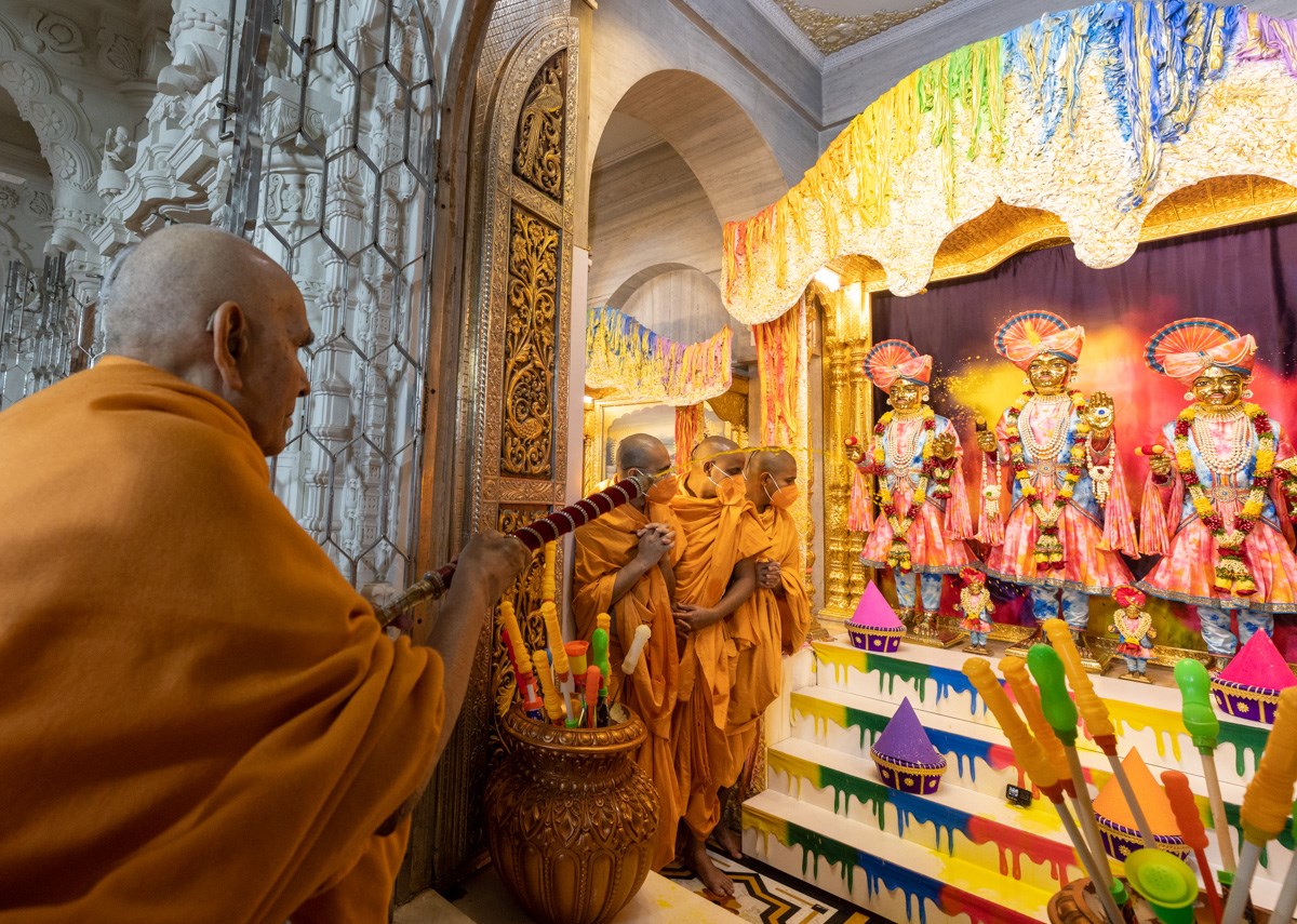 Swamishri sprays saffron-scented water on Bhagwan Swaminarayan, Aksharbrahma Gunatitanand Swami and Shri Gopalanand Swami