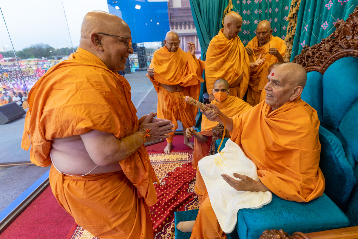 Swamishri sprays saffron-scented water on Pujya Ghanshyamcharan Swami