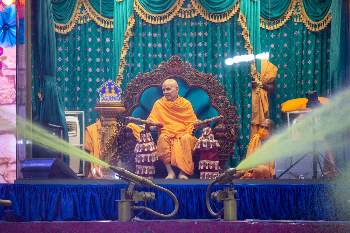 Swamishri sprays sanctified saffron-scented water on devotees
