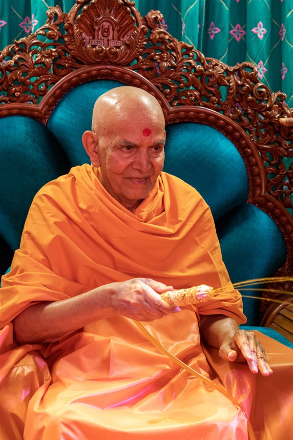 Swamishri sprays sanctified saffron-scented water