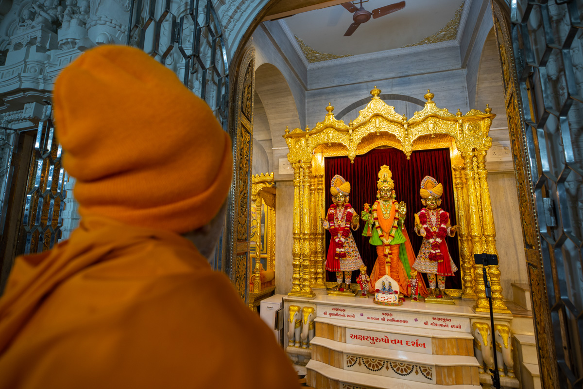 Swamishri engrossed in darshan of Bhagwan Swaminarayan, Aksharbrahma Gunatitanand Swami and Shri Gopalanand Swami