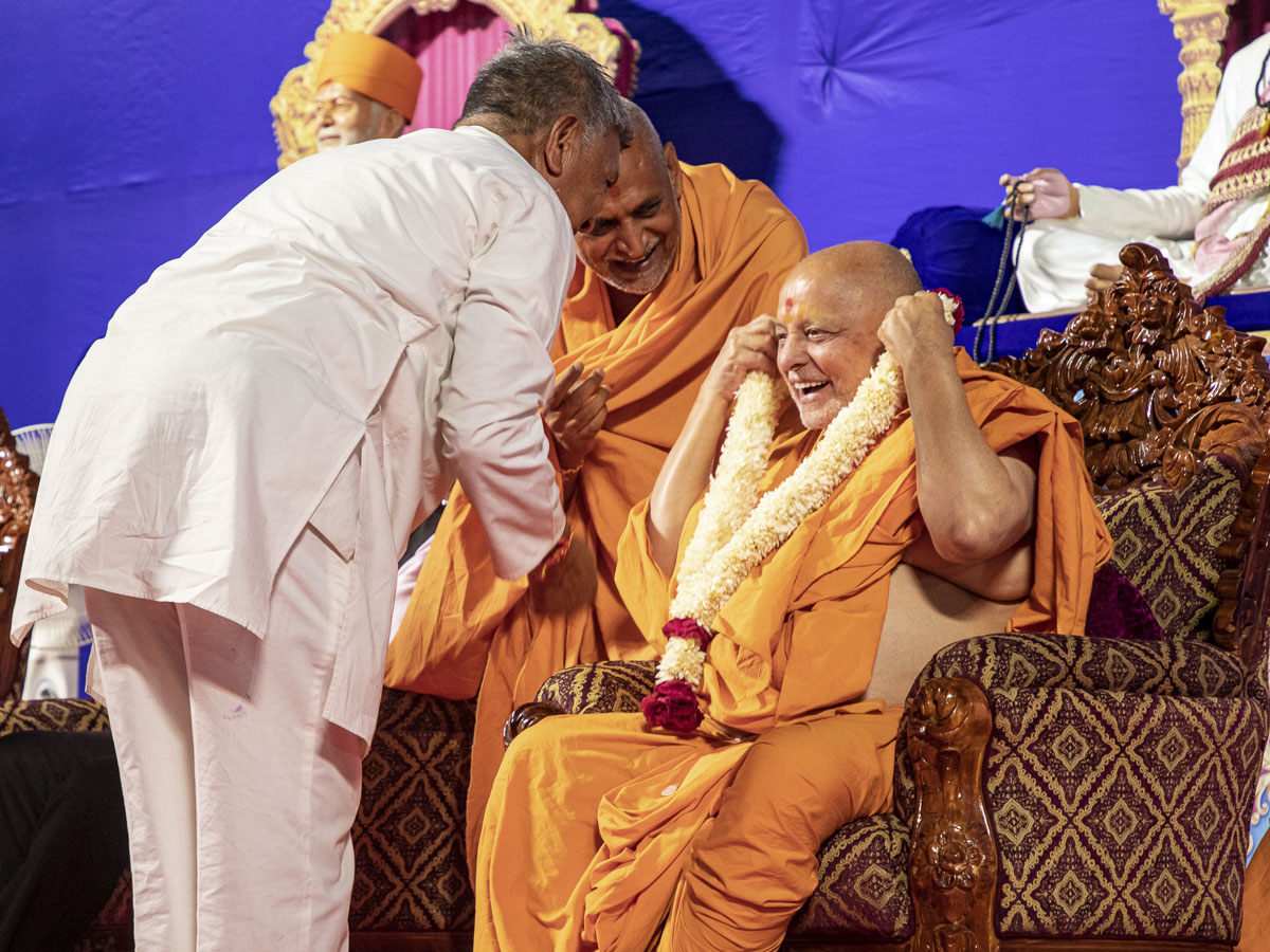 A devotee honors Pujya Ishwarcharan Swami with a garland