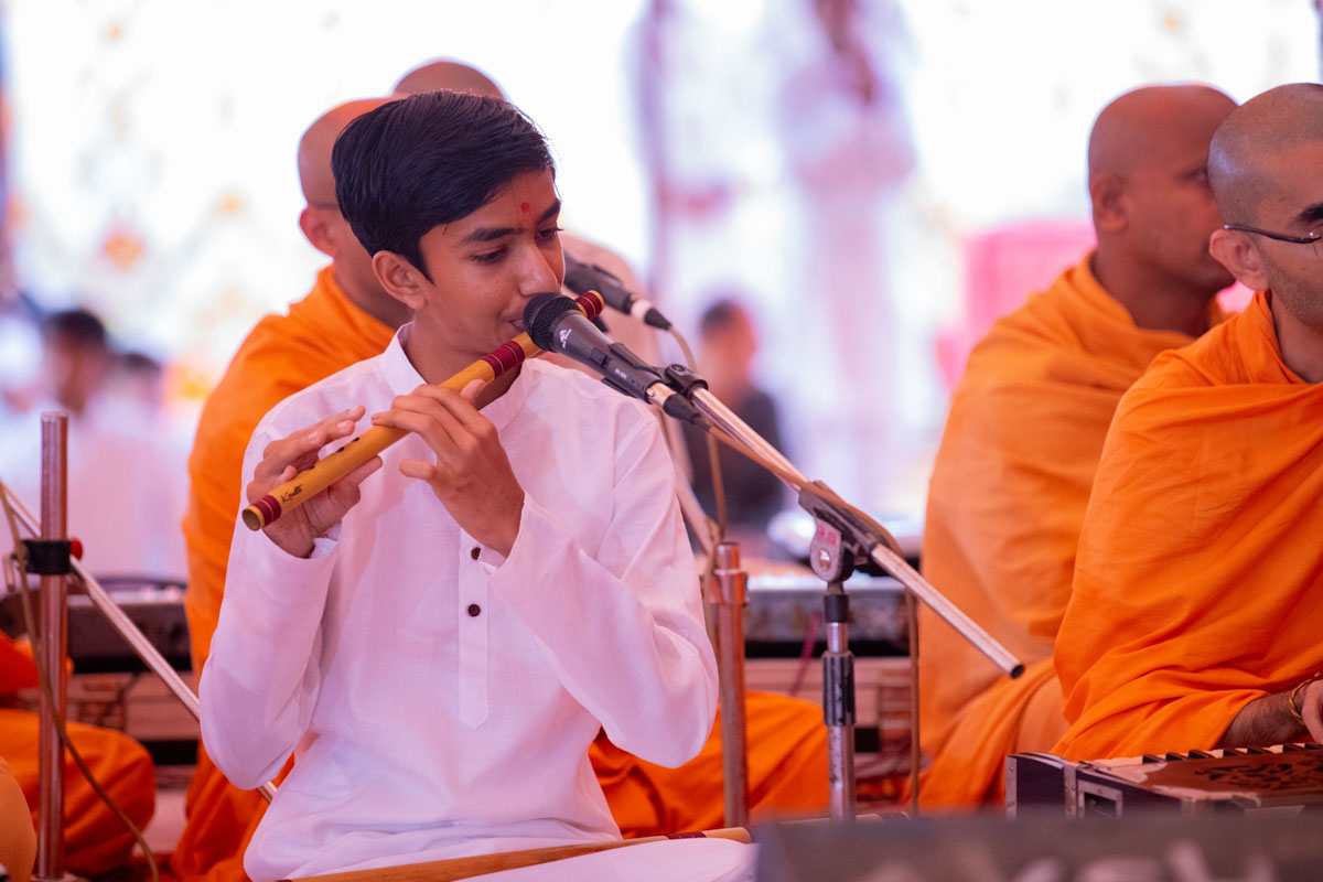 A youth plays the flute in Swamishri's daily puja