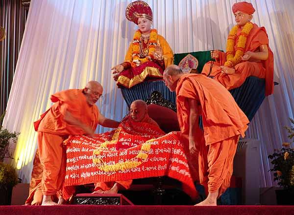 Pujya Viveksagar Swami and Pujya Ghanshyamcharan Swami present a shawl with the words of "Maha Balwant Maya Tamaari" on it