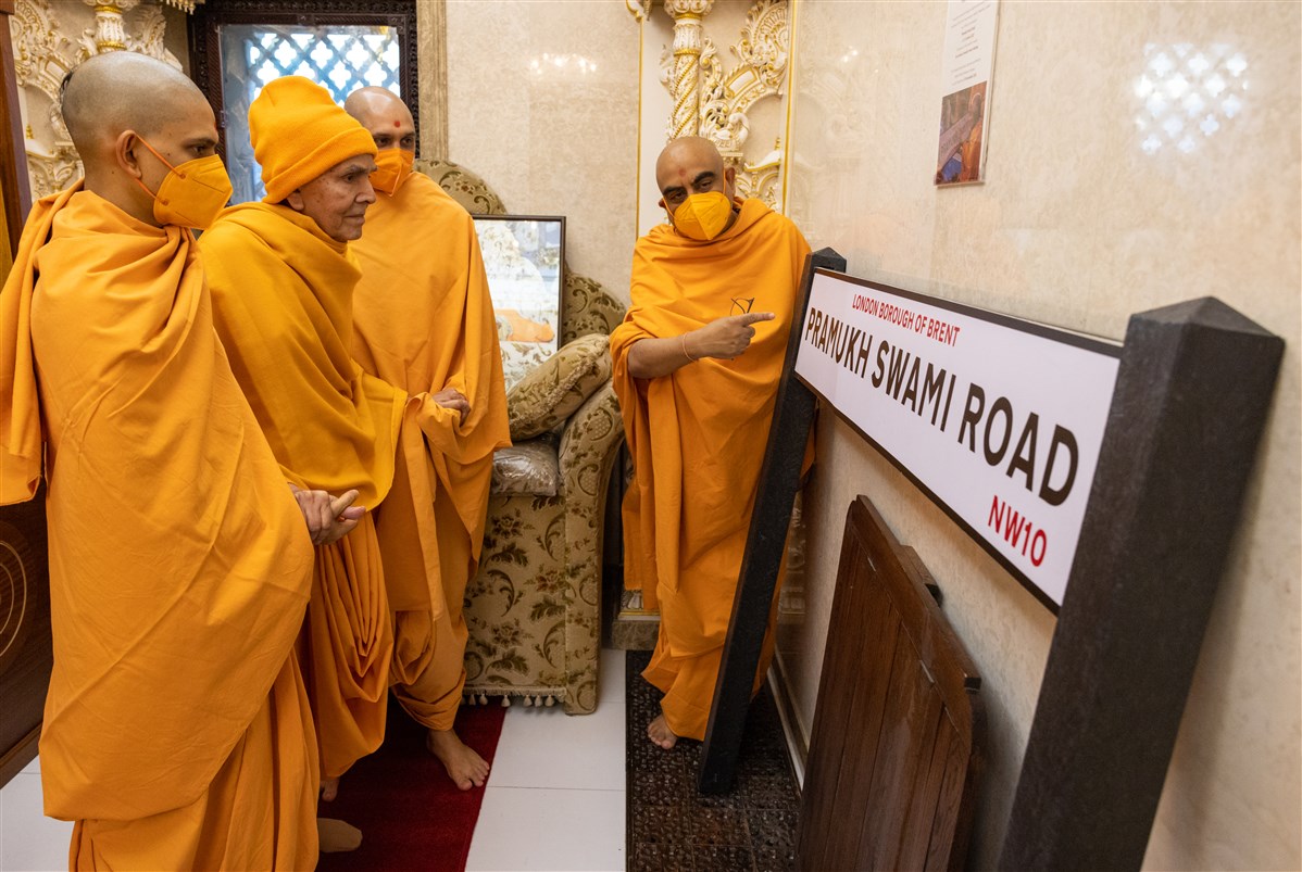 Swamishri observes the ‘Pramukh Swami Road’ sign sanctified by him in Nenpur, India, in 2020, after the previous road was renamed in honour of the creator of London Mandir<br>Learn more <a href='https://www.baps.org/News/2021/Pramukh-Swami-Road-in-Honour-of-the-Creator-of-Neasden-Temple-19549.aspx' target='blank' style='text-decoration:underline; color:blue;' >here</a>