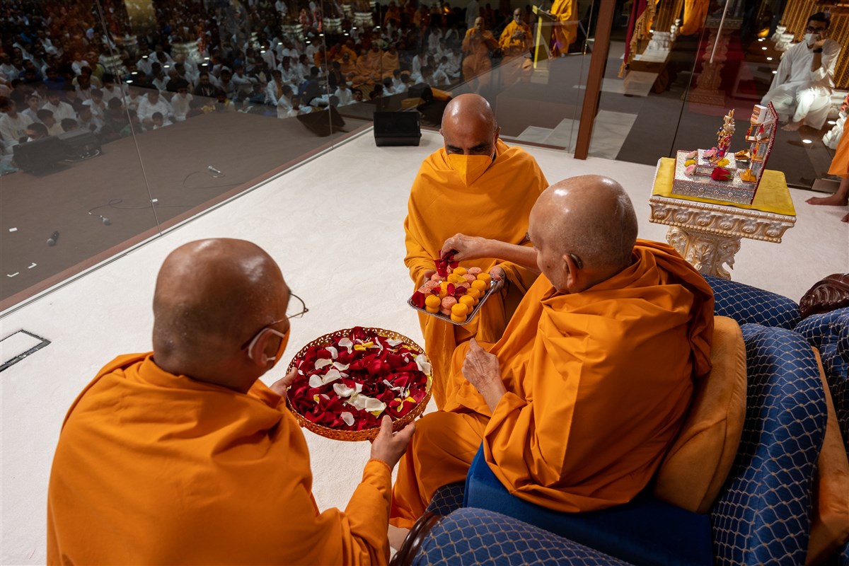 Swamishri sanctifies pendas with flower petals for devotees to enjoy as prasad