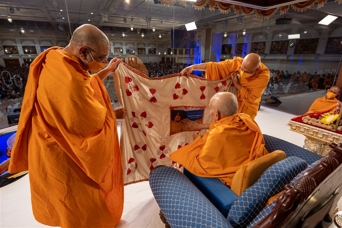 Bhaktivallabhdas Swami and Tyagprakashdas Swami present to Swamishri a decorative shawl depicting the Satsang Diksha
