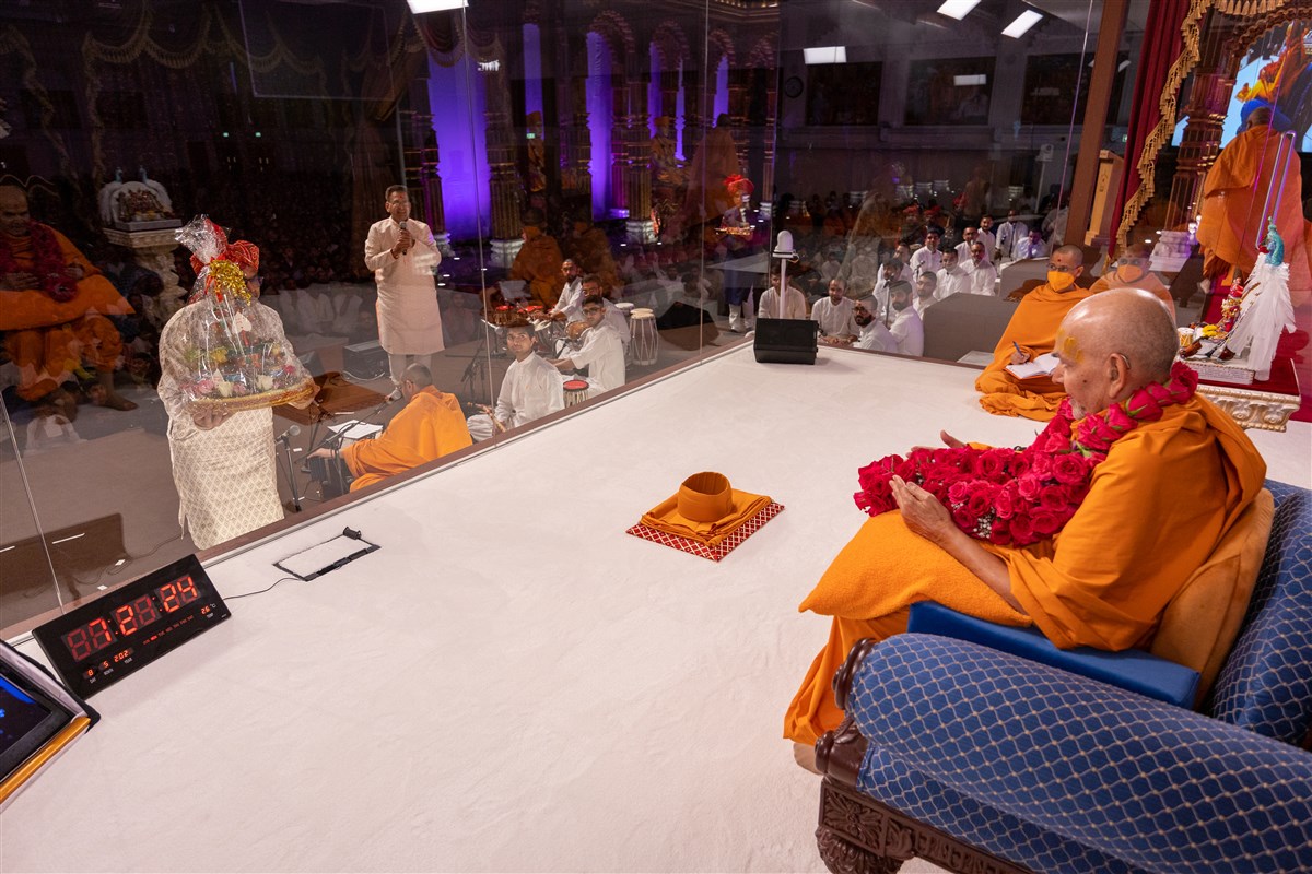Devotees offer gifts to Thakorji and Swamishri as swamis continue the lyrics of welcome and praise