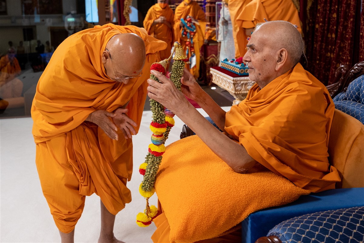 Swamishri blesses Tyagvallabhdas Swami on his diksha anniversary with the sanctified garland