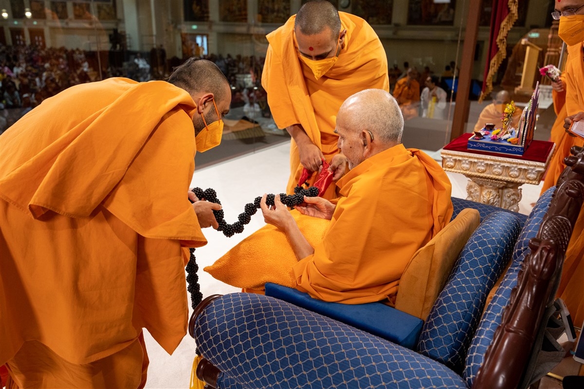 Tyagratnadas Swami and Paramsetudas Swami honour Swamishri with a decorative garland hand-crafted from beads