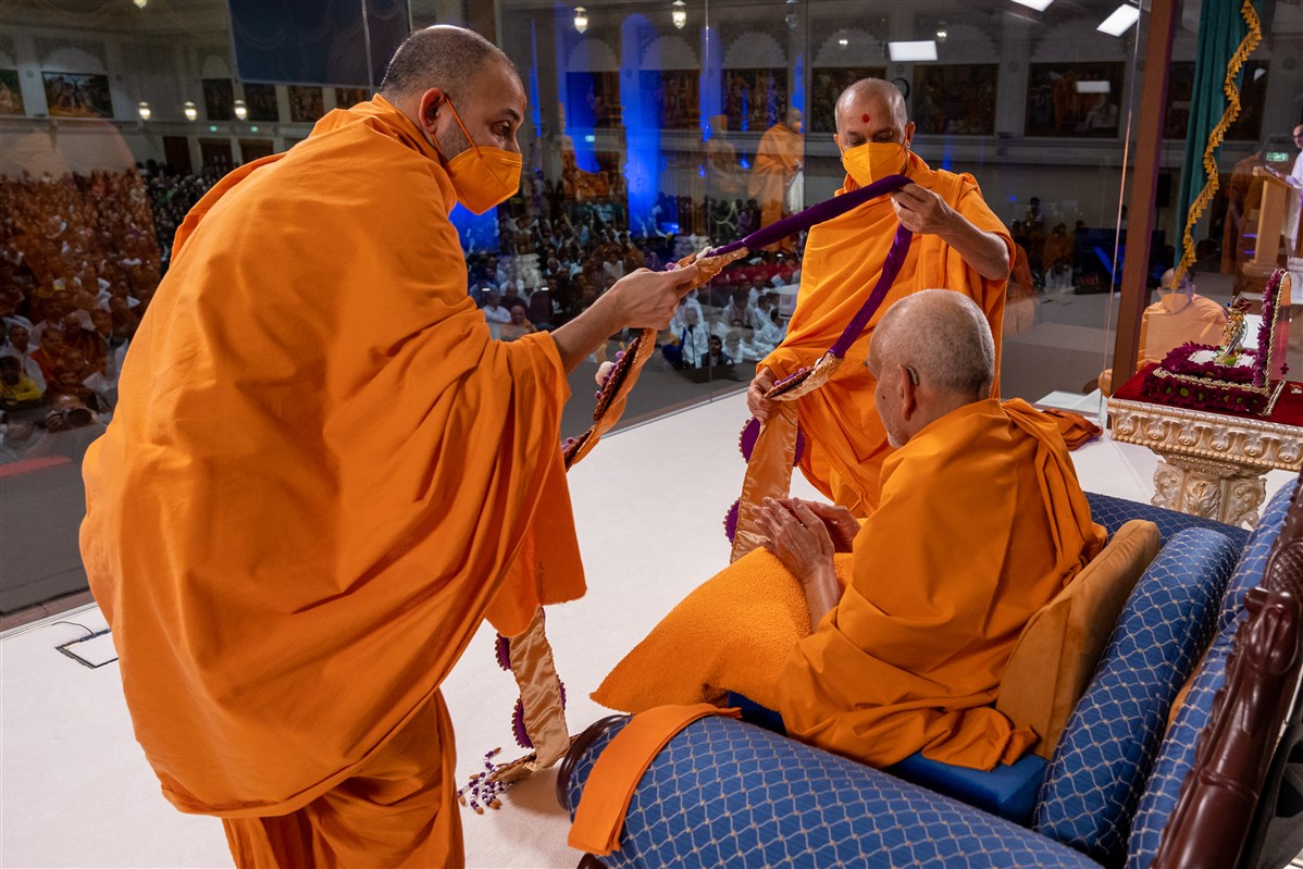 Munibhushandas Swami and Taponishthadas Swami offer Swamishri a decorative garland made by the mahilas
