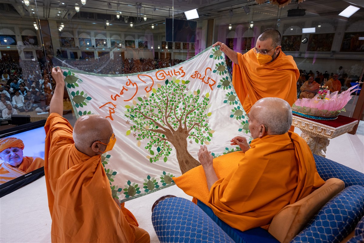 Tyagprakashdas Swami and Yogikirtandas Swami present Swamishri with a decorative shawl reiterating the theme of Karyakar Din, '<i>Mare Banvu Chhe Upasak Karyakar'</i>, based on a letter written by Swamishri