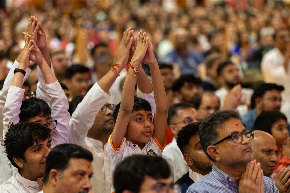 Children and devotees fold hands as Swamishri departs the assembly hall <br>To learn more about Karyakar Din, please click <a href='https://www.baps.org/News/2023/Mare-Banvu-Chhe-Upasak-Karyakar--Karyakar-Din-23543.aspx' target='blank' style='text-decoration:underline; color:blue;'>here</a>