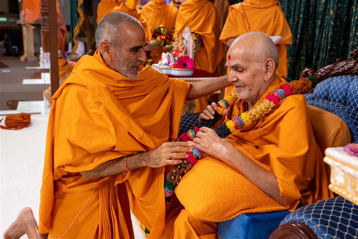 Anandswarupdas Swami honours Swamishri with a decorative garland with dry fruits
