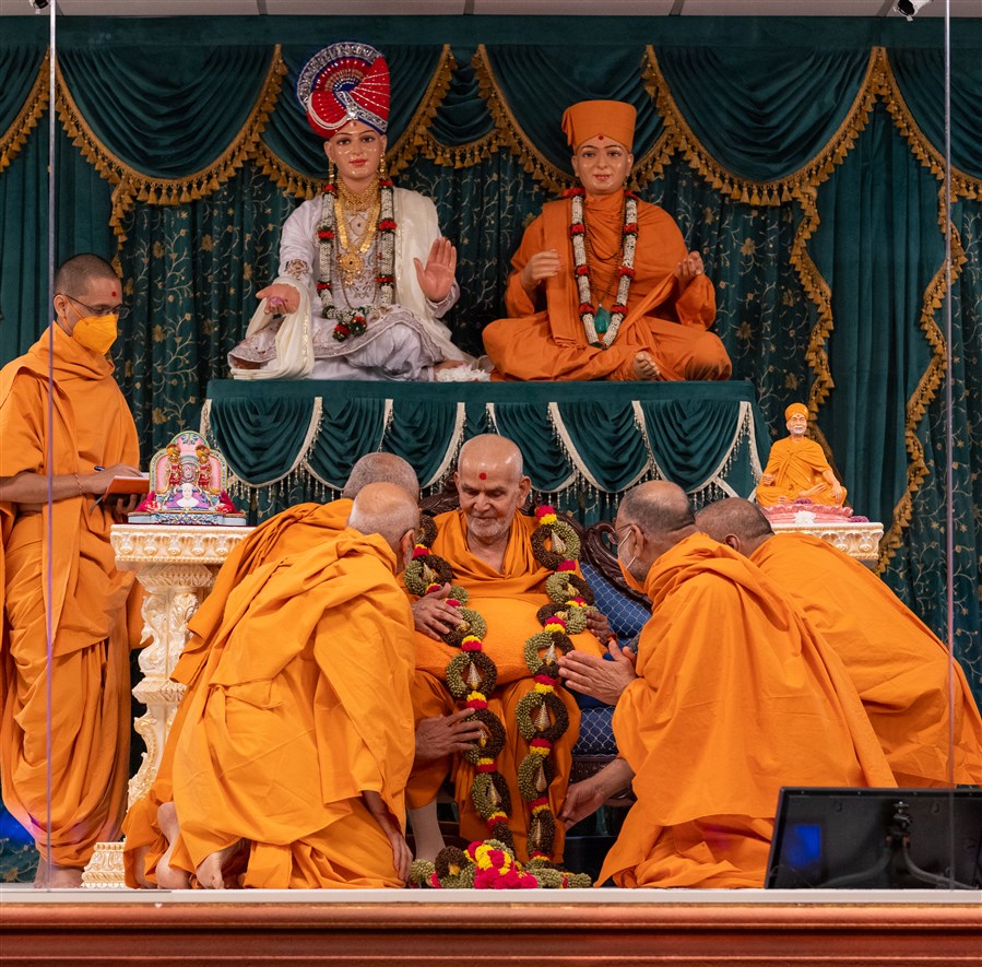 Swamis honour Swamishri with a decorative garland of cardamom and cloves