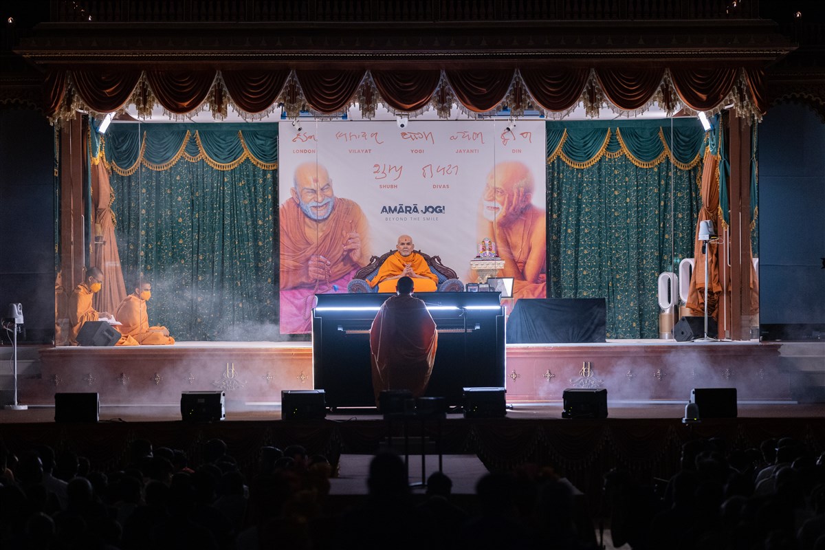 Swamishri is greeted in the assembly by a kirtan evoking the divine form of Yogiji Maharaj