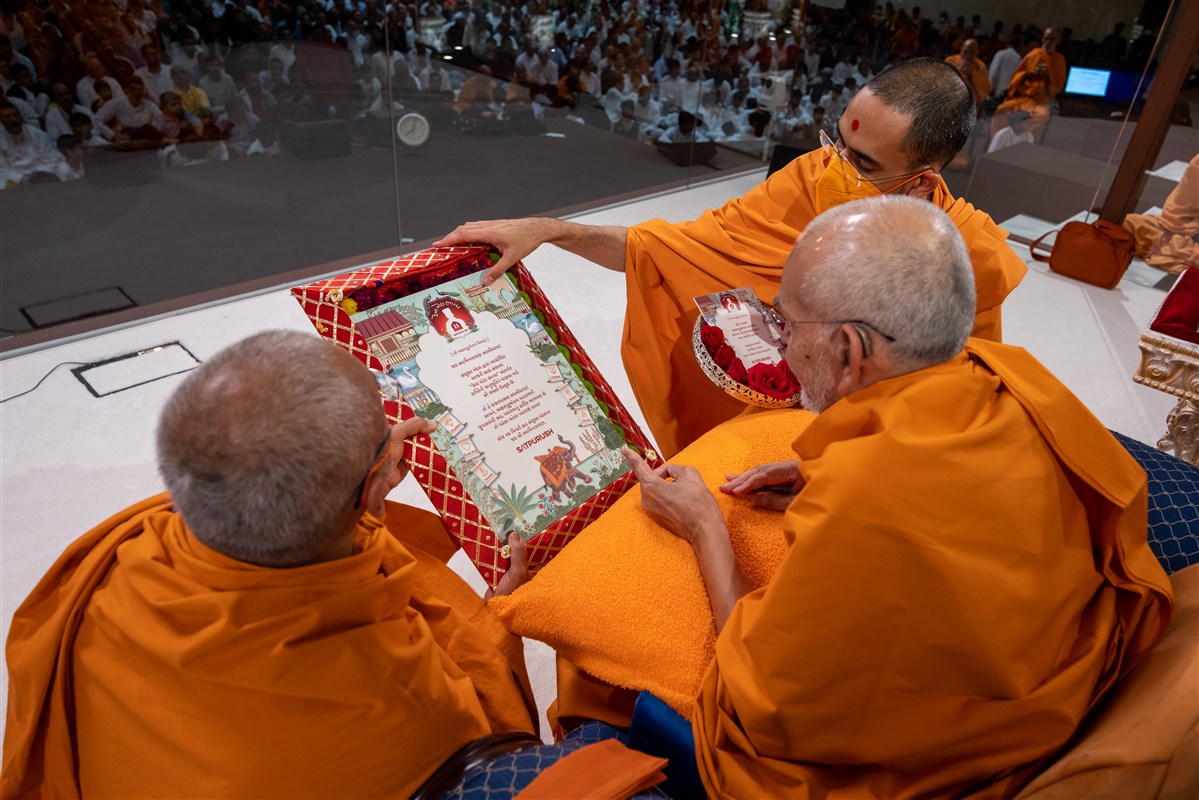Prabuddhmunidas Swami and Paramtattvadas Swami offer a decorative card to Thakorji and Swamishri inviting them to bless the evening programme