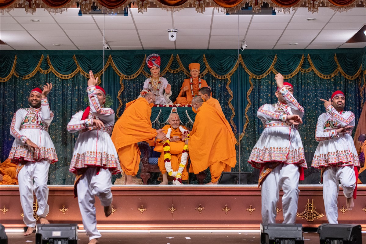 Bhaktivallabhdas Swami and Anandpriyadas Swami welcome Swamishri to the assembly with a garland of fresh flowers