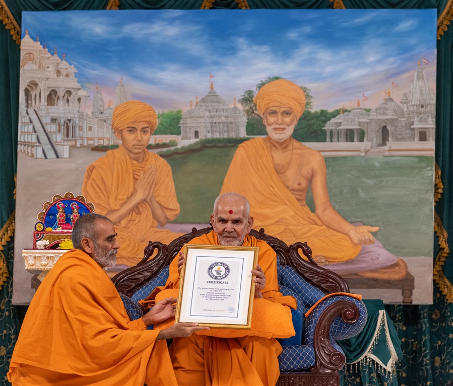 Swamishri presents the certificate to the assembly <br>To learn more about the world record-making bubble wrap portrait, please click <a href="https://www.baps.org/News/2022/Bubble-Wrap-Portrait-of-Pramukh-Swami-Maharaj-Recognised-as-Guinness-World-Record-23127.aspx" target="blank" style="text-decoration:underline; color:blue;">here</a>