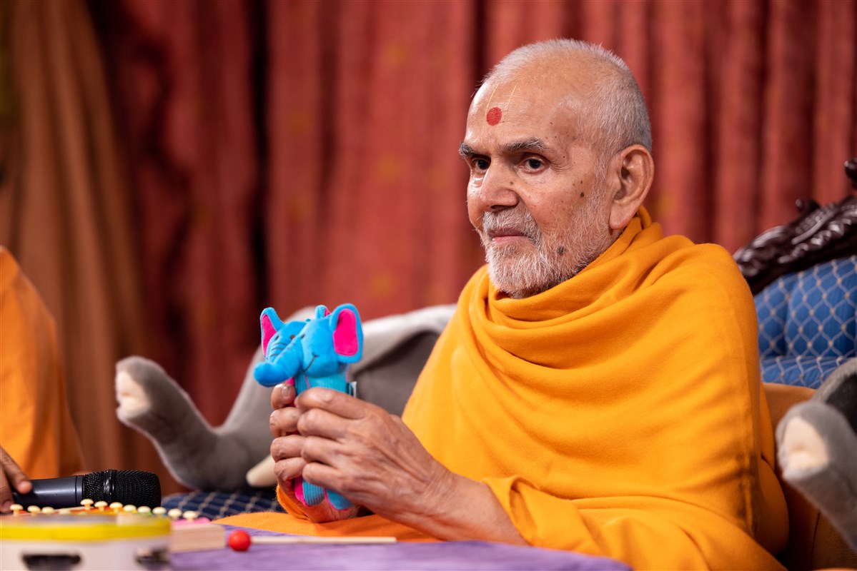 Swamishri plays a pair of toy rattles as a part of the interactive game with the children