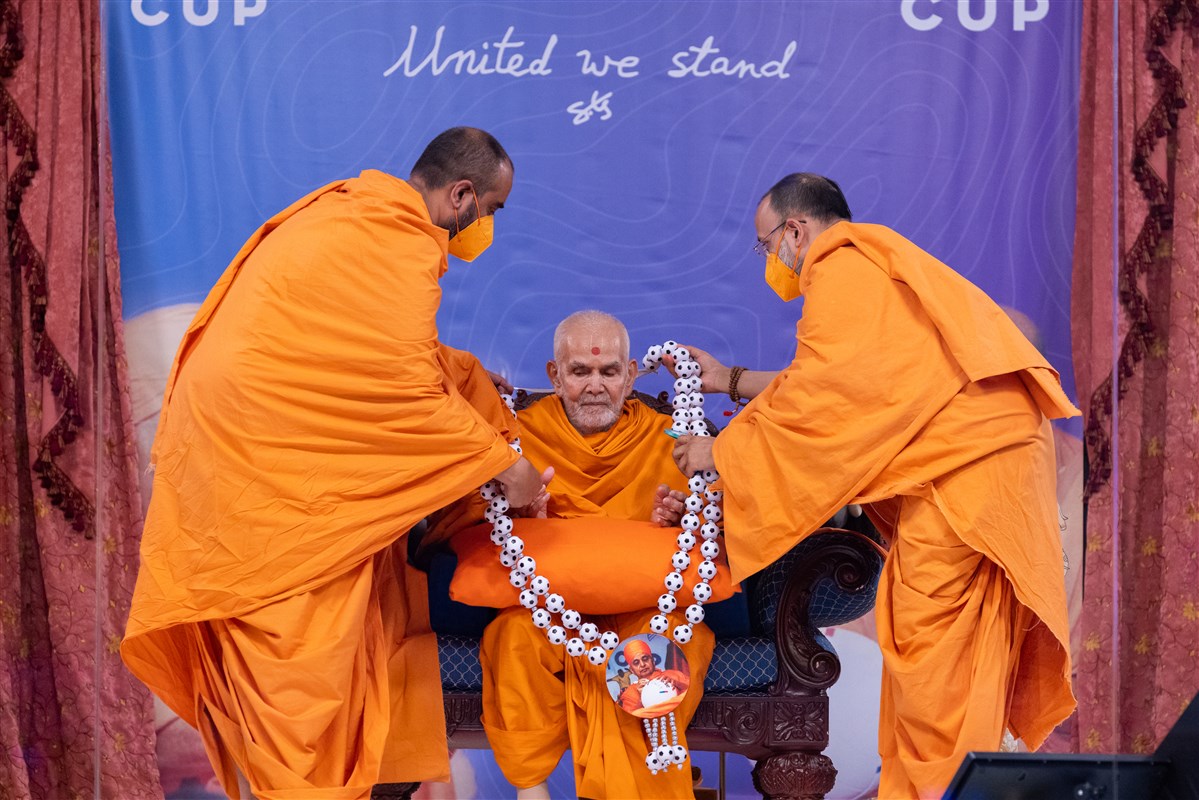 Yagnatilakdas Swami and Manoharmurtidas Swami honour Swamishri with a decorative football garland