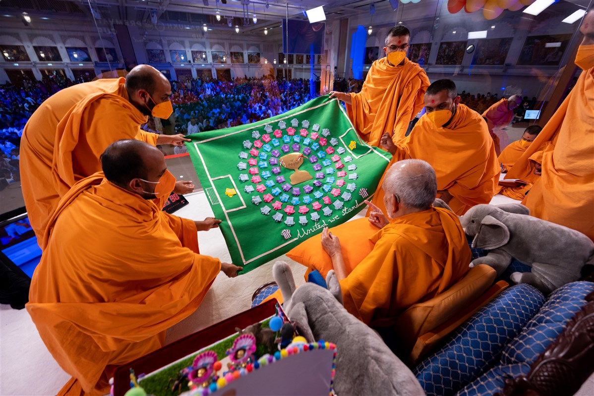 Swamis offer Swamishri a football-themed decorative shawl