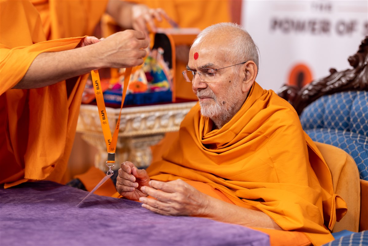 Swamishri is presented with an ID badge to join the day's proceedings as a delegate