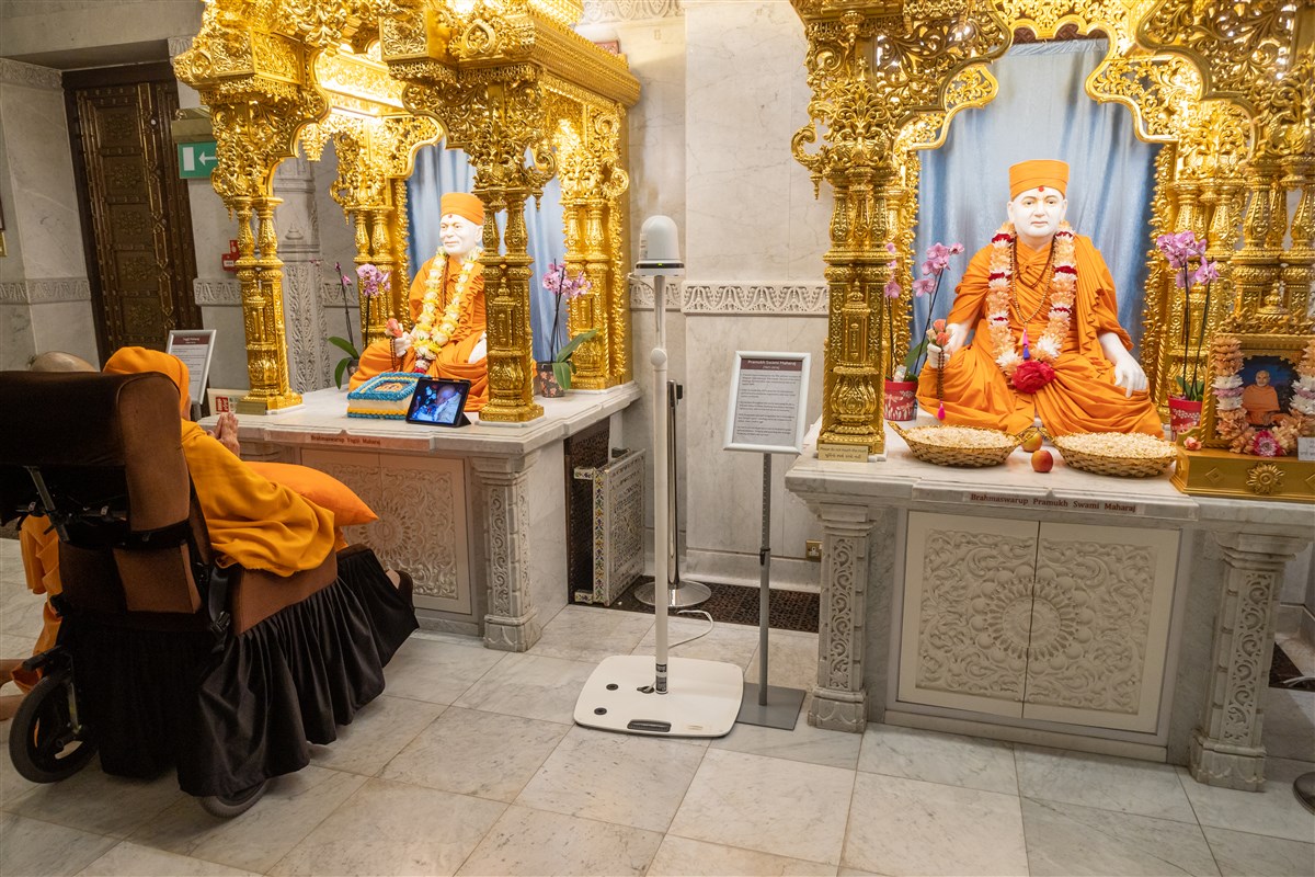 Swamishri engrossed in the darshan of Yogiji Maharaj, while also observing video footage of Yogiji Maharaj in London on 3 June 1970, exactly 53 years ago, where he is offered a cake <br>(Watch clip <a href='https://youtu.be/s0SaLGEBBMM?t=5645' target='blank' style='text-decoration:underline; color:blue;'>here</a>)