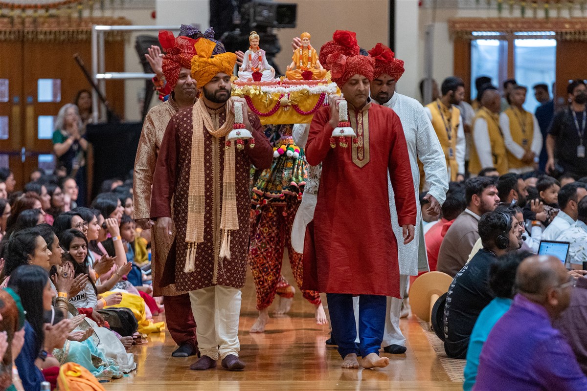 Devotees carry murtis of the Guru Parampara into the hall on a decorated open palanquin