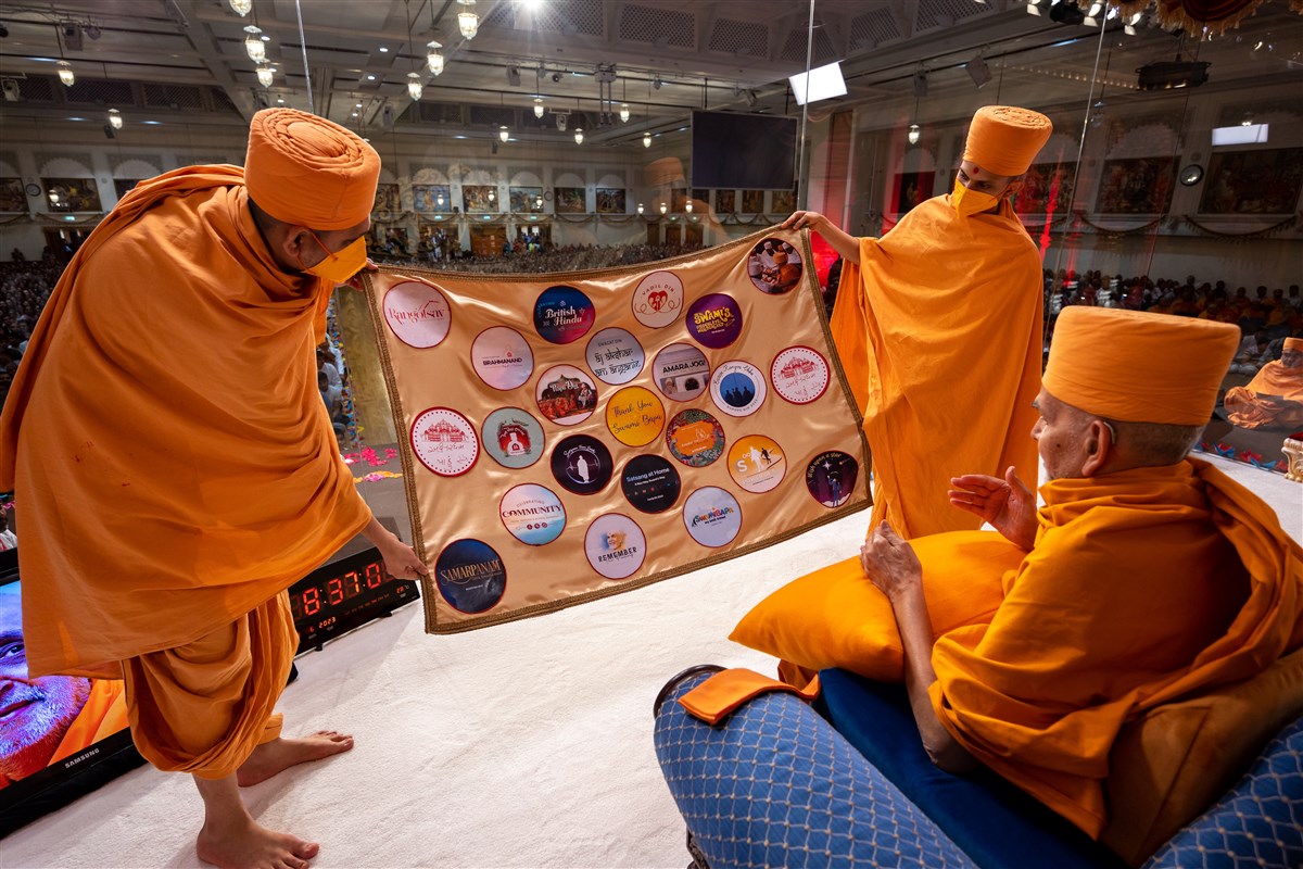Shrutipriyadas Swami and Uttamyogidas Swami present a decorative shawl highlighting the various programmes celebrated during Swamishri's 38-day visit