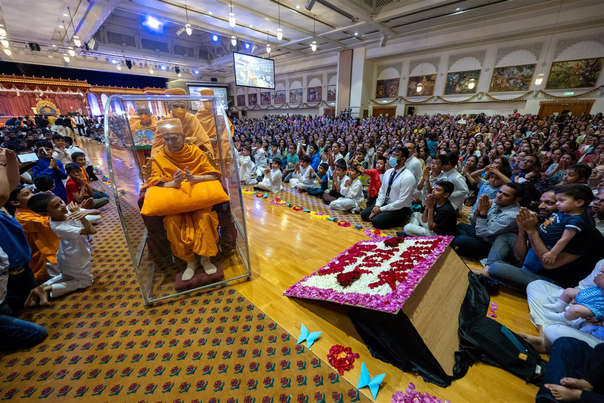 Swamishri greets the devotees with folded hands as he passes through the assembly