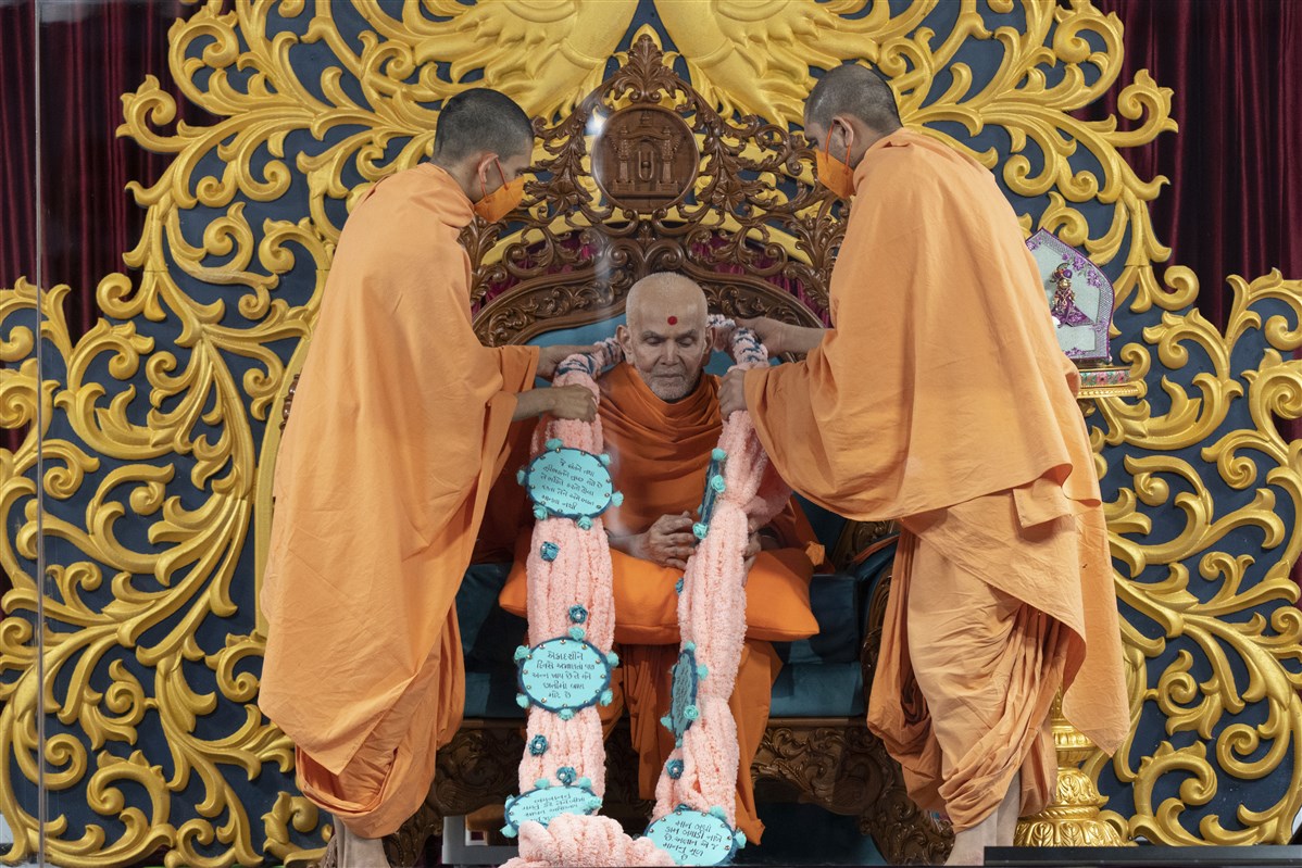 Swamishri being presented with a lovingly crafted  garland with verses from 'Purushottam Bolya Prite'