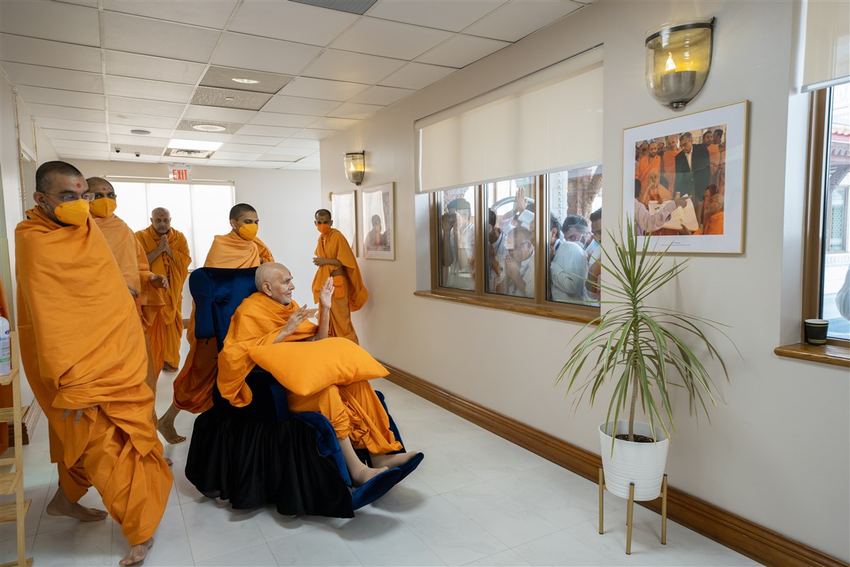 Swamishri bestows blessings upon devotees as they do darshan through the window