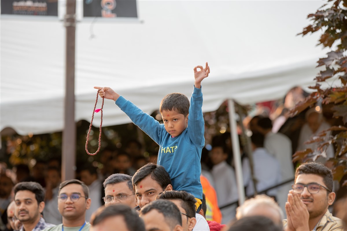 A young devotee is engaged in turning mala, his gaze fixated on Swamishri