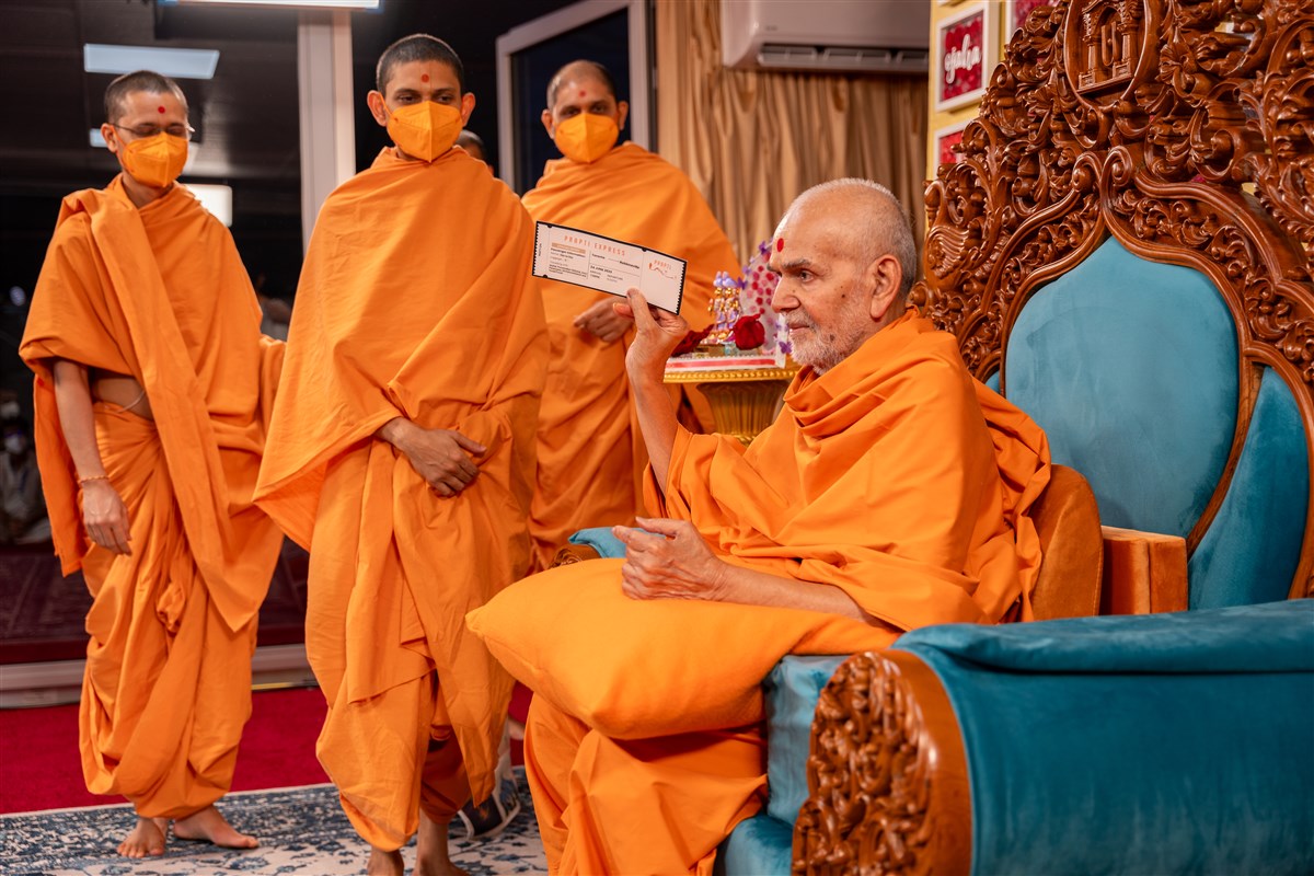 Swamishri sanctifies a boarding pass for the evening Prapti Din assembly