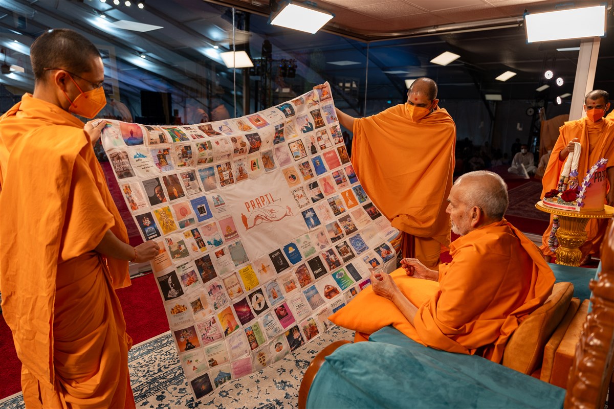 Swamishri observes a decorative shawl outlining the theme of the Prapti Din celebrations