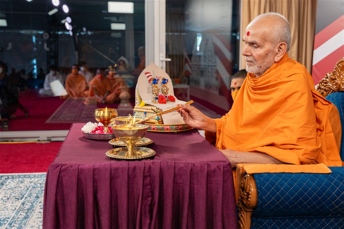 Swamishri takes flame from the lamp ignited using the sunrays and uses it to ignite two other lamps to mark the launch of the Festival of Inspirations to be celebrated in Robbinsville, New Jersey