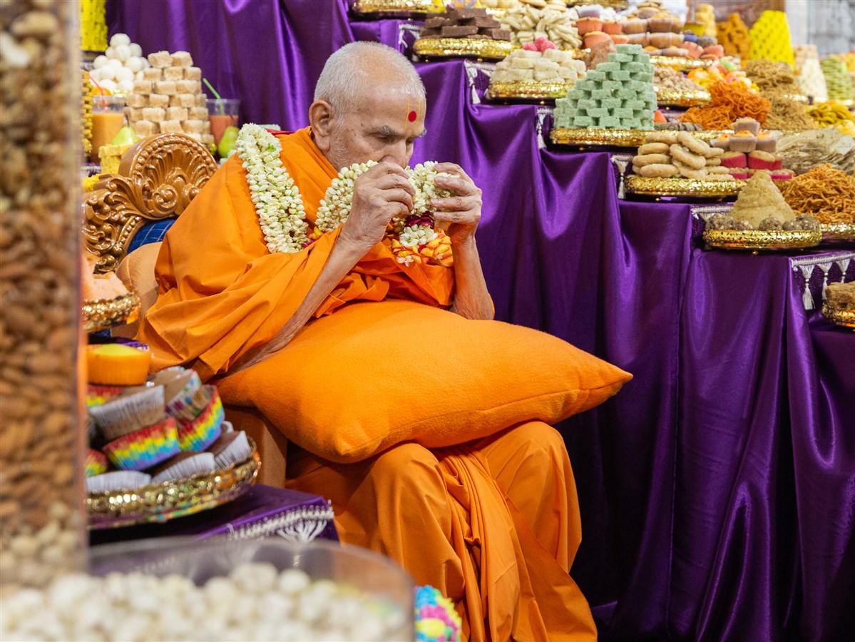 Swamishri reverently presses the jasmine garland against his eyes as a heartfelt gesture of gratitude