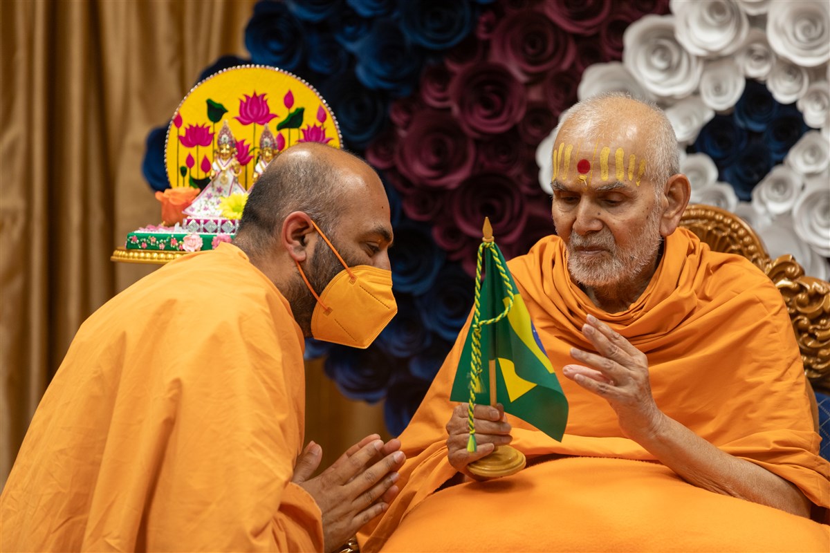 Holding the flag of the Republic of Brazil, Swamishri blesses Priyasevadas Swami