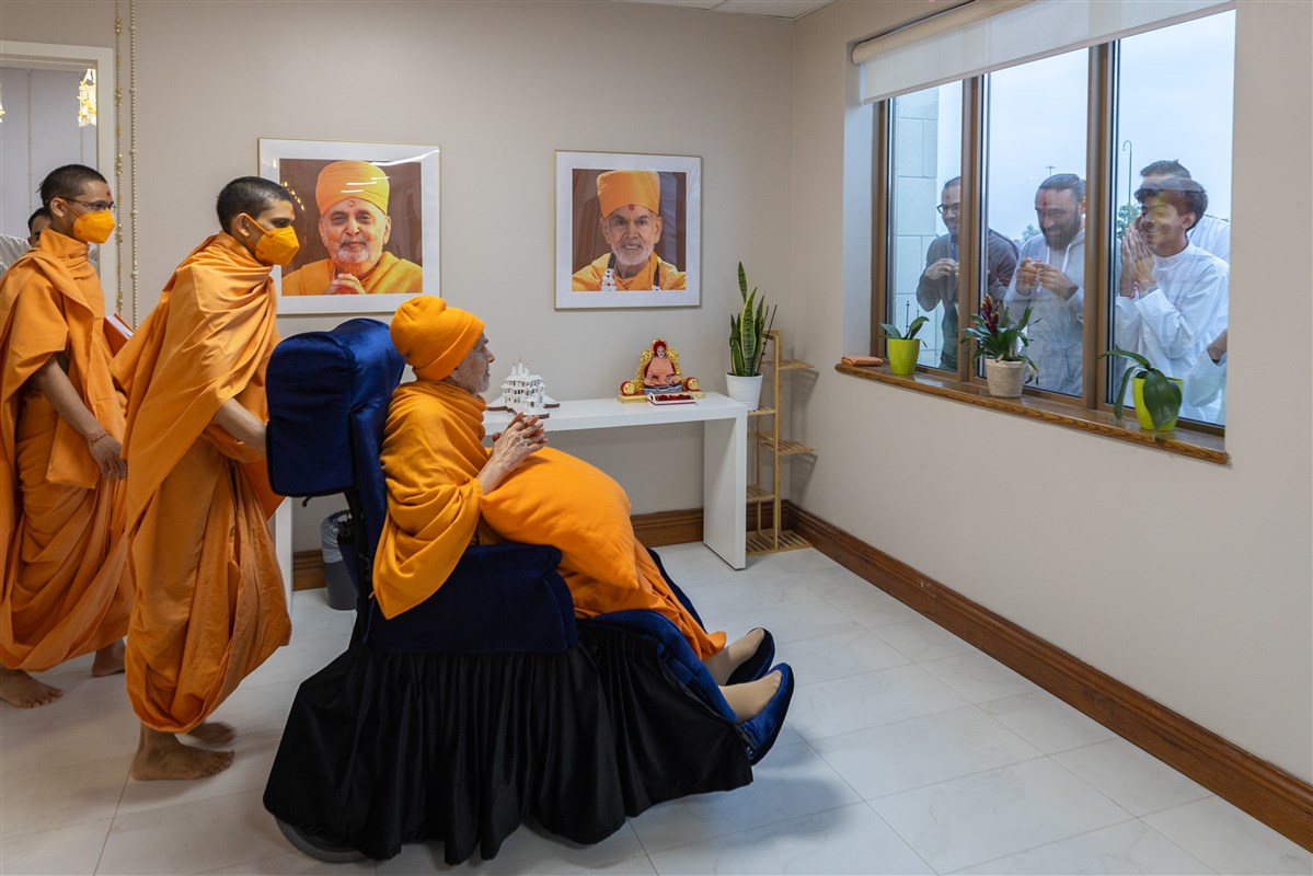 As Param Pujya Mahant Swami Maharaj moves through the corridor for Thakorji's darshan, devotees get a quick glimpse of him