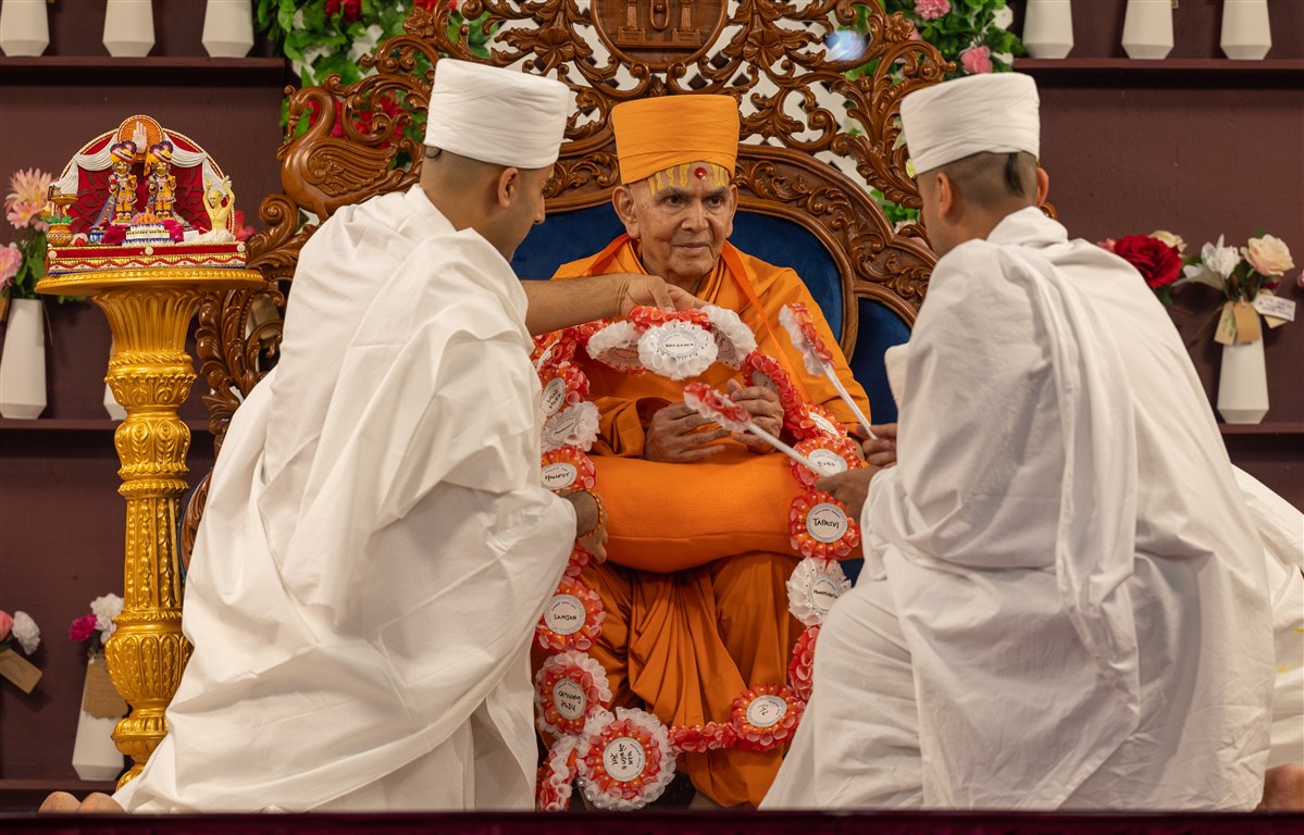 The new parshads offer Swamishri a decorative garland and chhadi